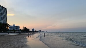 Una playa con un paseo curvo, edificios al fondo y gente caminando por la orilla.