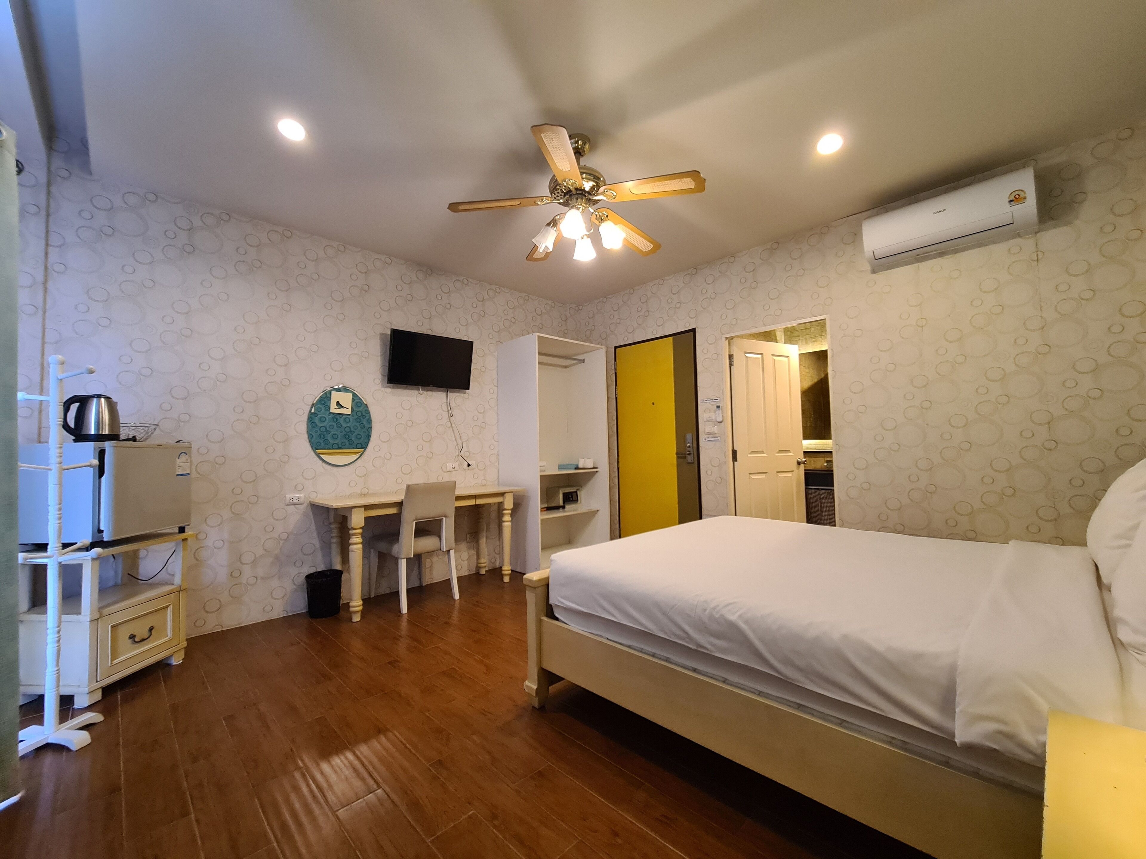 A bedroom with a bed, a desk, a chair, a ceiling fan, a TV, and an air conditioning unit.