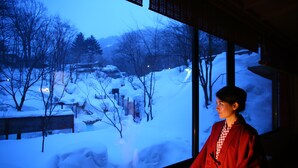 A person standing in front of a large window with a snowy landscape view. - Awanoyu (Matsumoto)