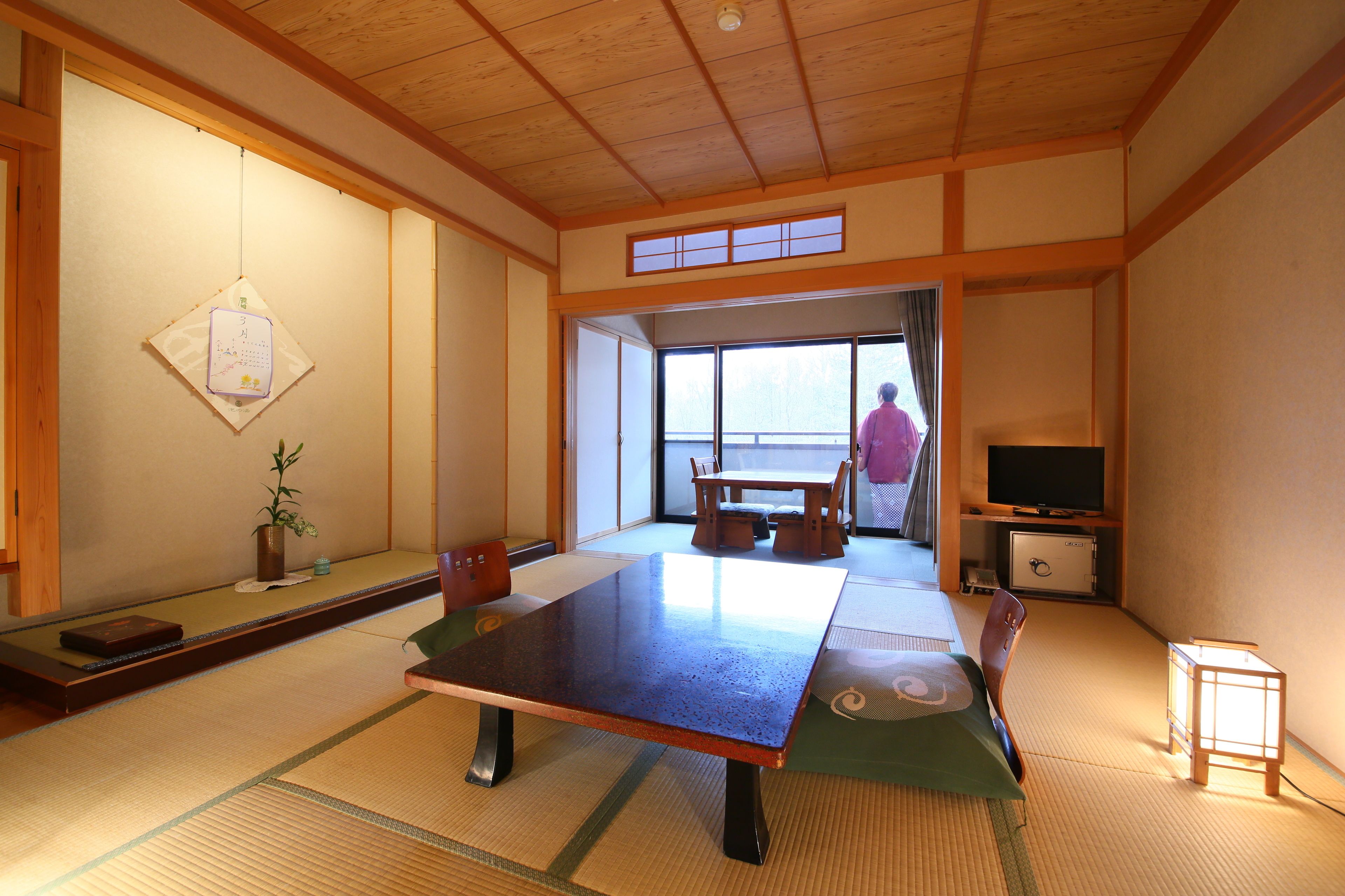 Una habitación tradicional japonesa con suelo de tatami, una mesa baja, un televisor y una puerta corrediza que da a un espacio al aire libre.