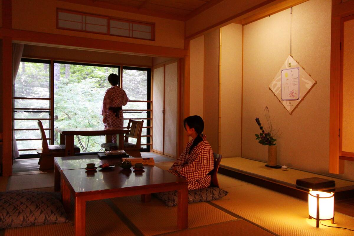 A traditional Japanese room with tatami flooring, a low table, and a sliding door leading to a garden.