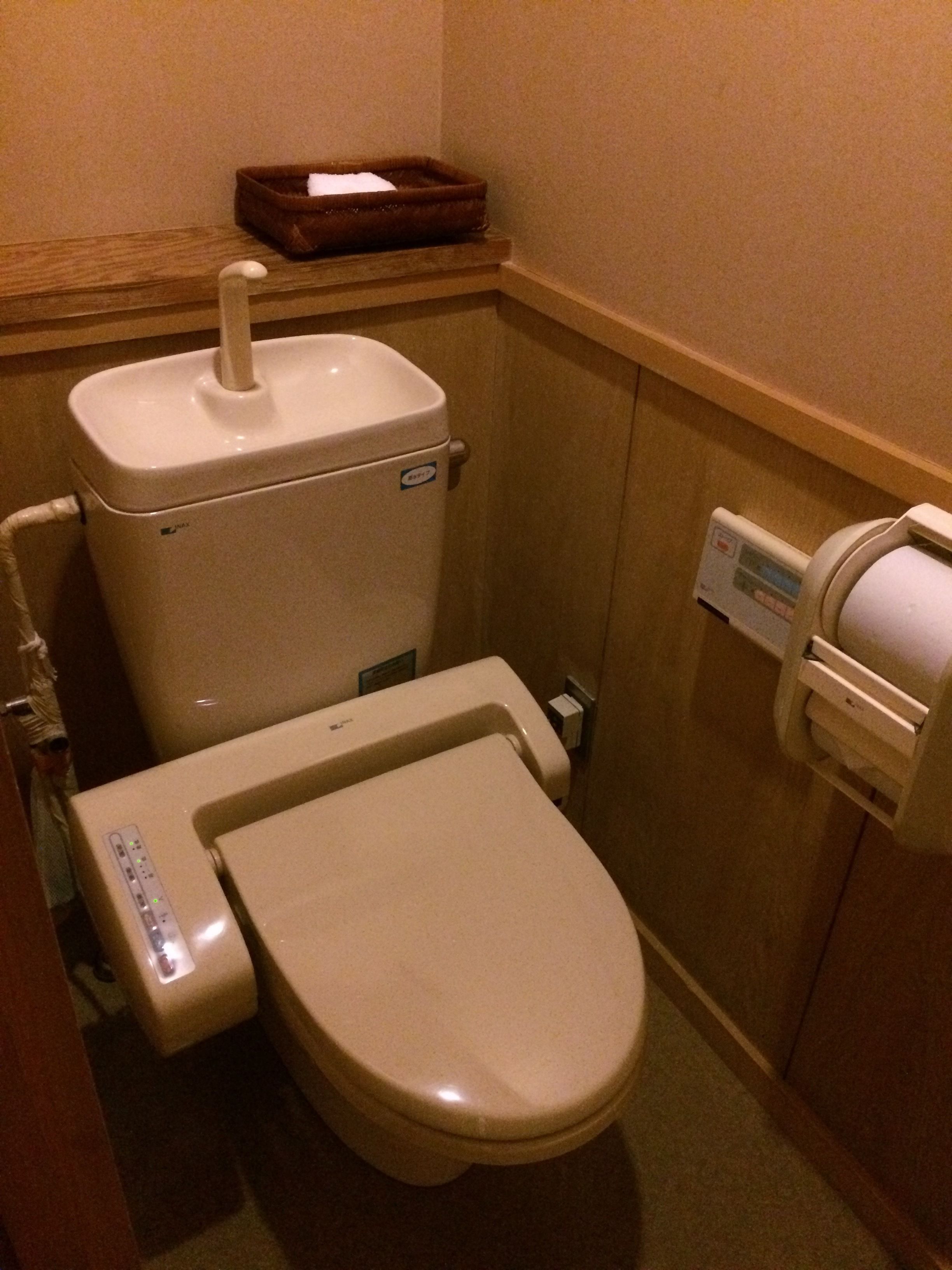 Et lille, kompakt badeværelse med toilet, bidet og en papirhåndklædedispenser.