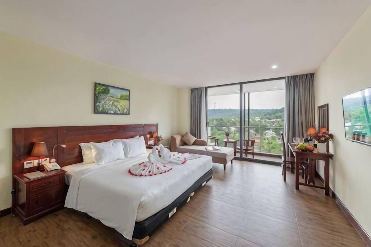 Une chambre d’hôtel avec un grand lit, un bureau, une chaise, une table de chevet et une vue sur l’extérieur.