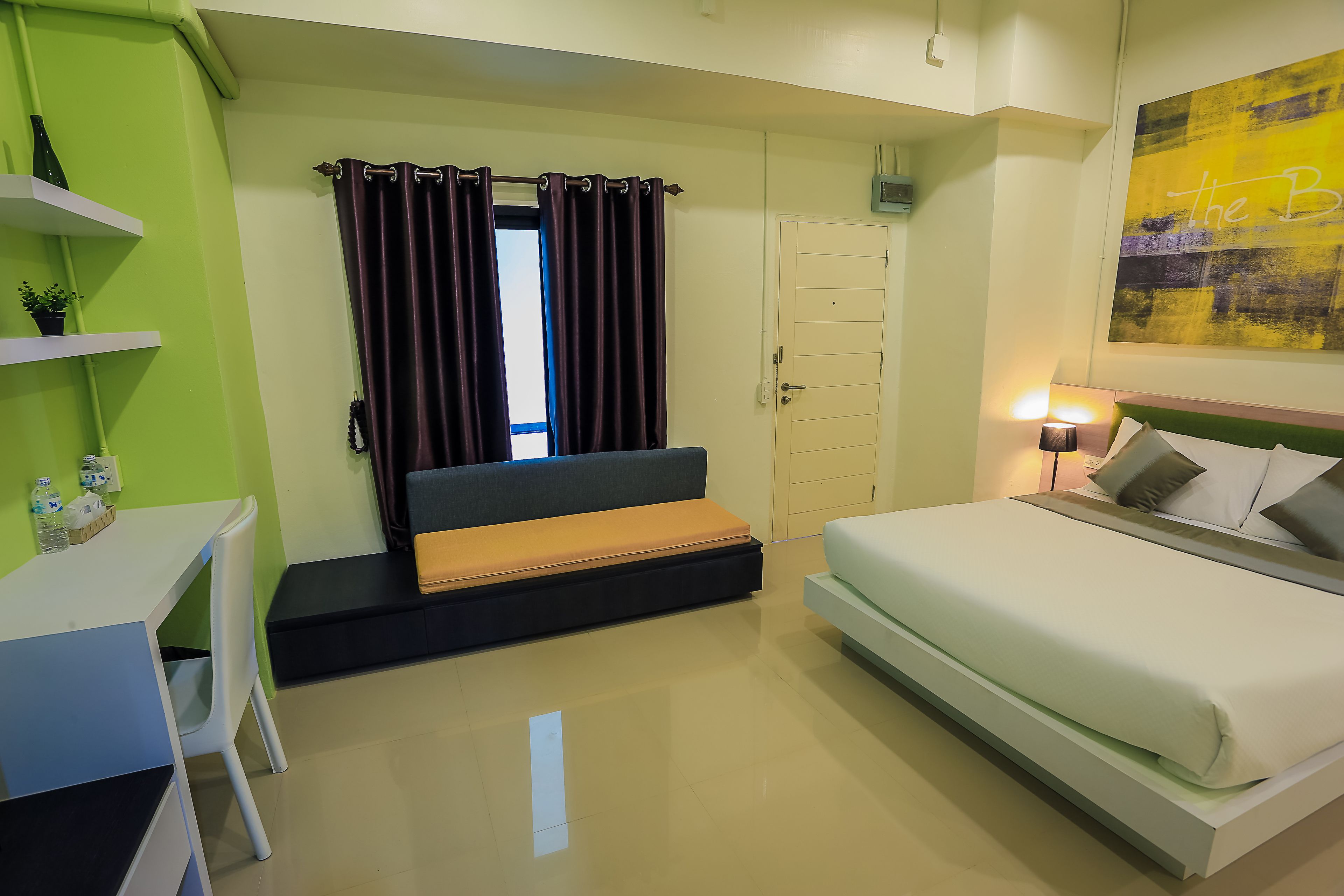 A compact hotel room with a bed, a desk, and a small seating area.
