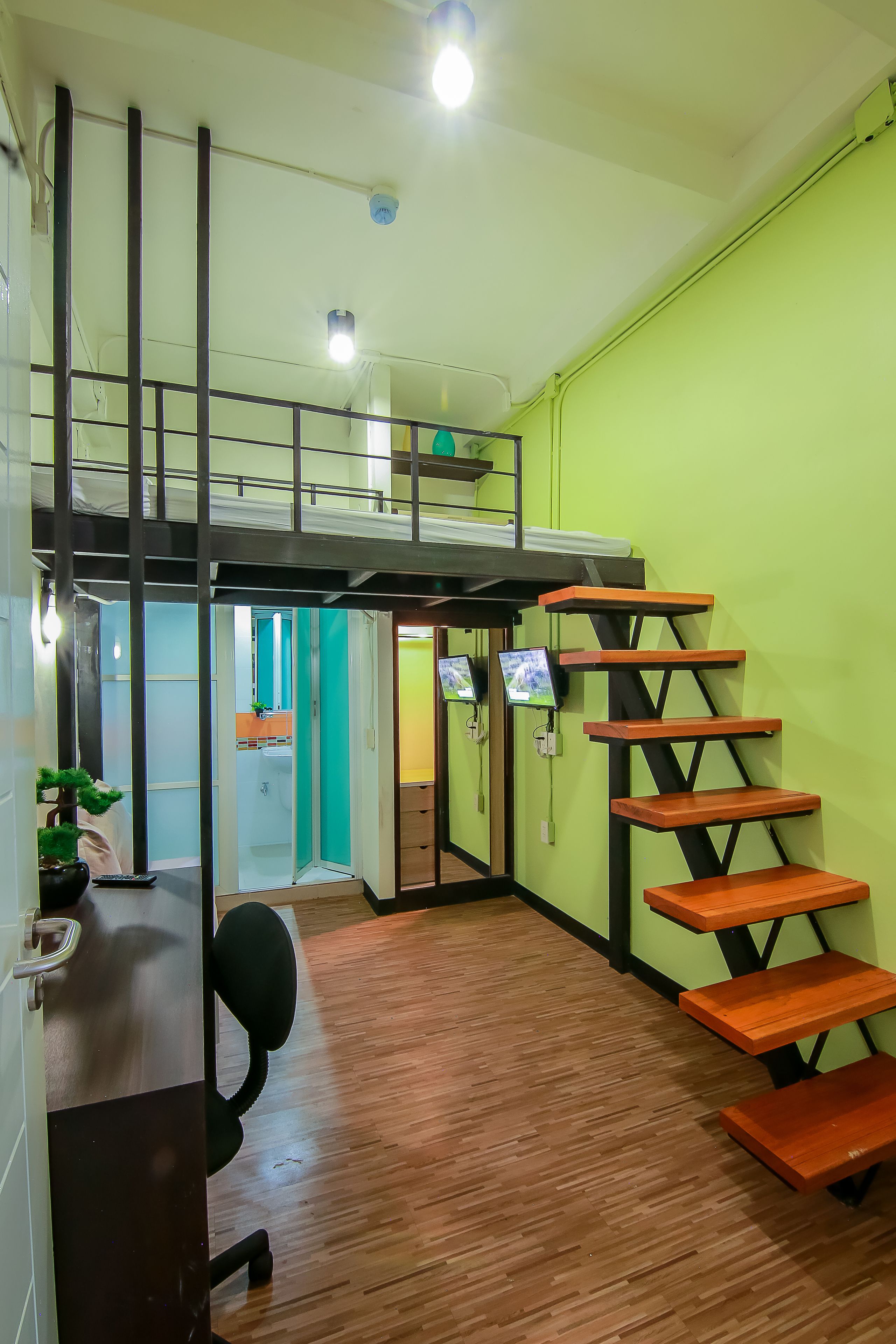 A room with a wooden floor, a staircase with wooden steps, a desk with a chair, and a green wall.