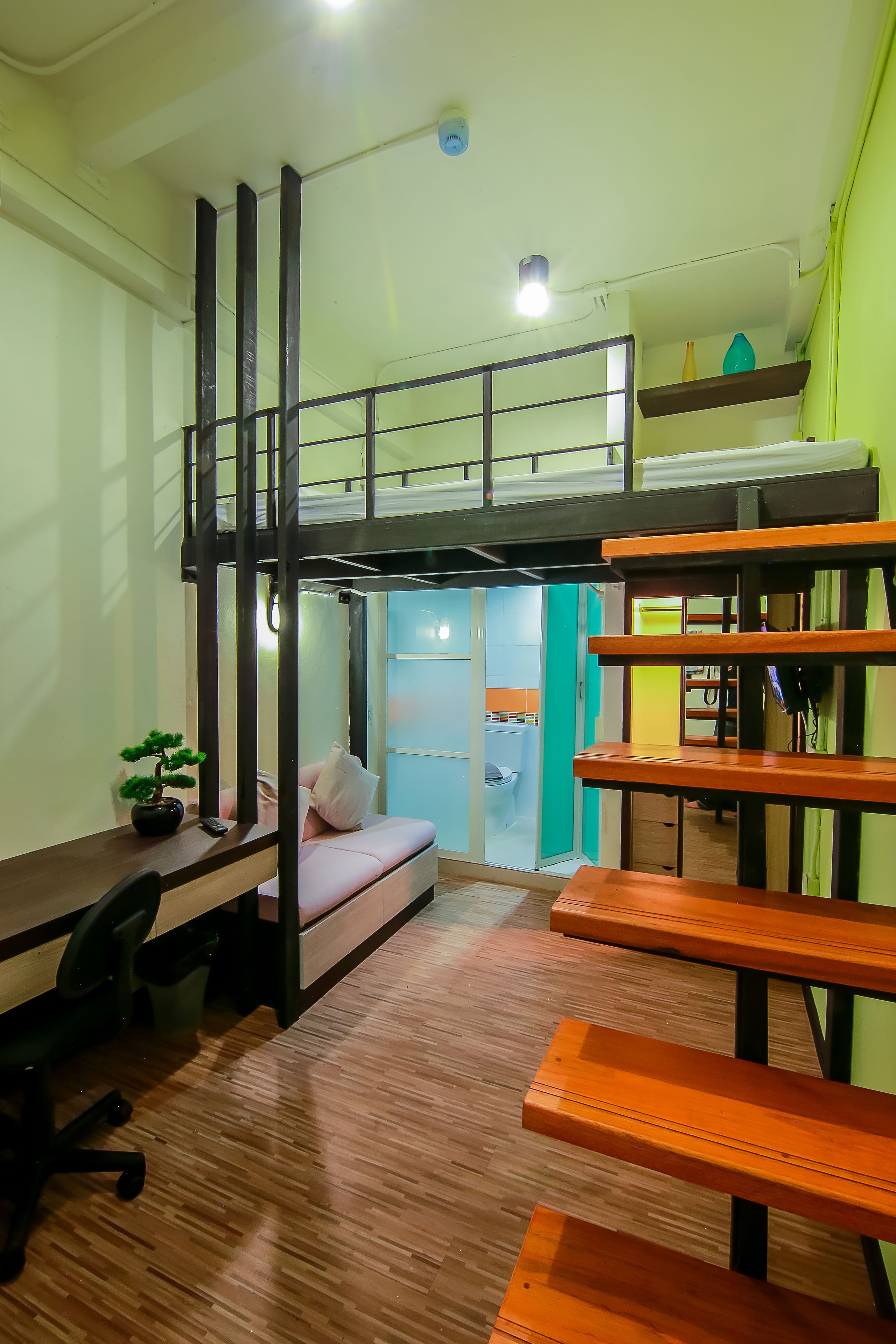 A compact dormitory room with a bunk bed, a desk with a chair, and a small potted plant.