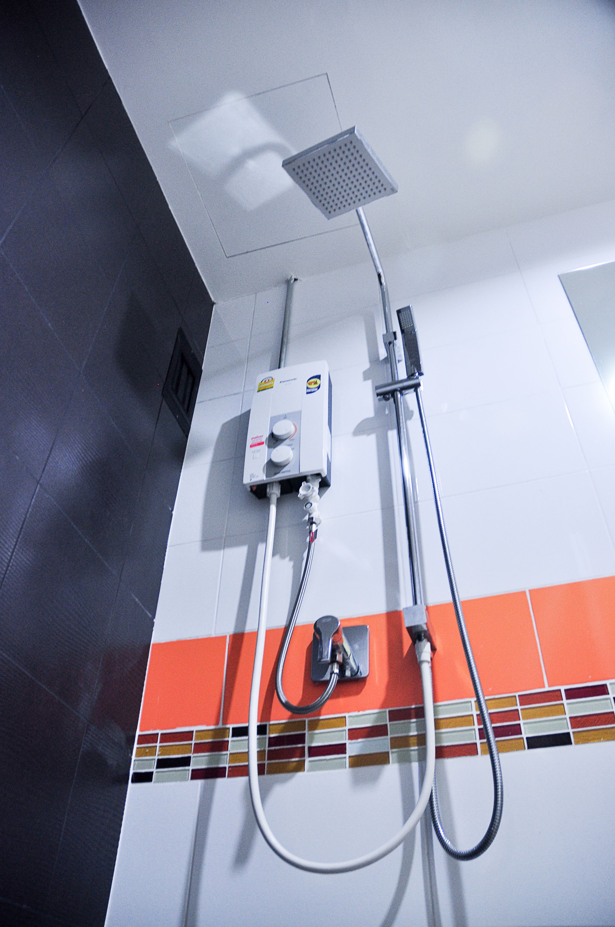 A shower area with a control panel, a handheld showerhead, and a hose.