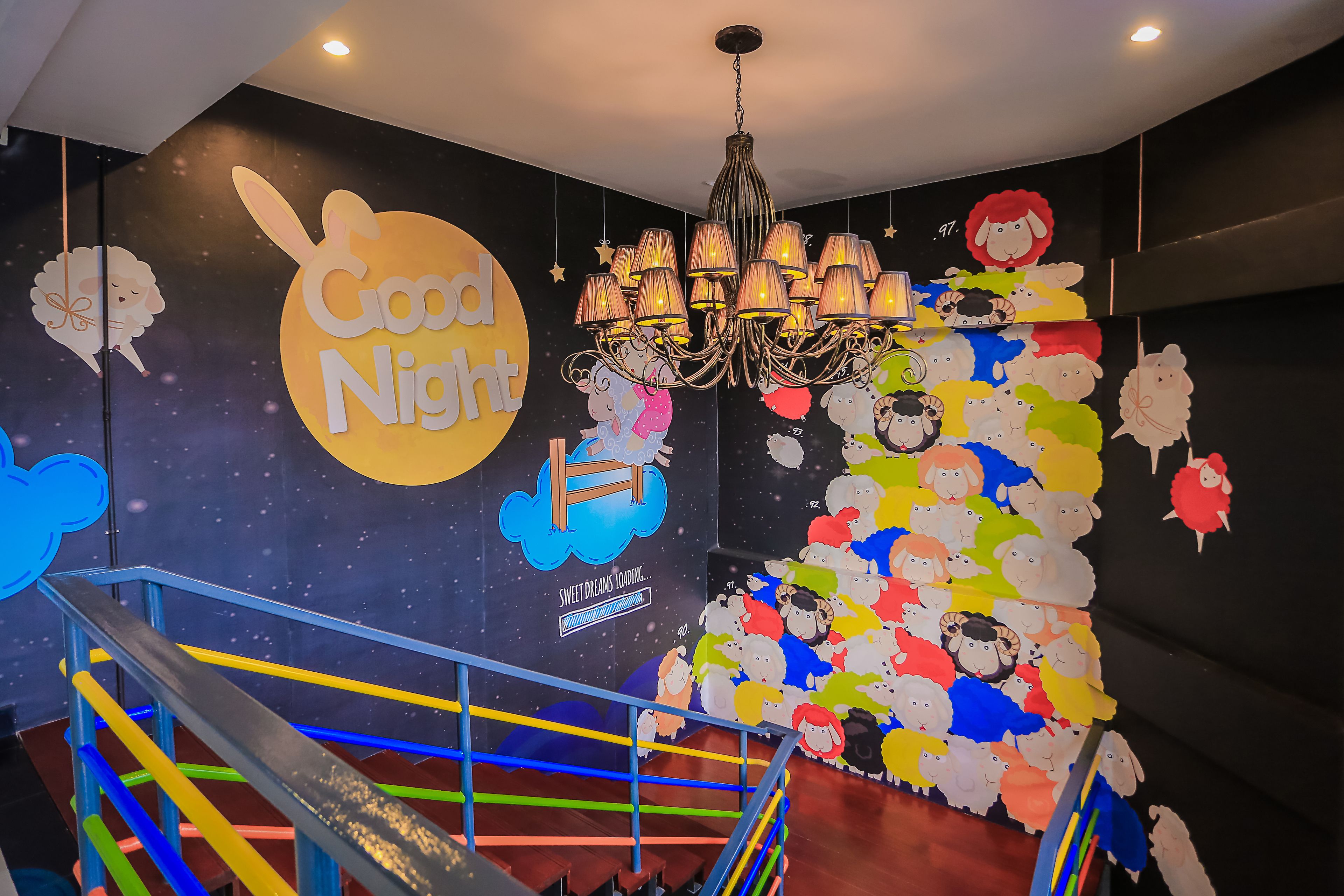 Una escalera con barandas de colores y una pared decorada con un cartel que dice 'Good Night' y un mural de ovejas.