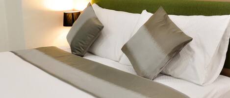 Una cama bien hecha con ropa de cama blanca y gris, un cabecero verde y una lámpara de noche.