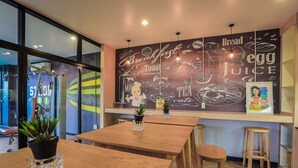 Een café-interieur met houten tafels, potplanten en een muurschildering met ontbijtproducten.