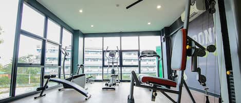 A gym with various exercise equipment, large windows, and a view of buildings outside.
