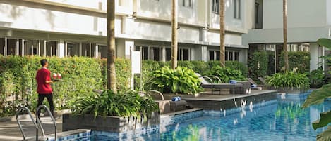 A swimming pool with lounge chairs and a person carrying trays.