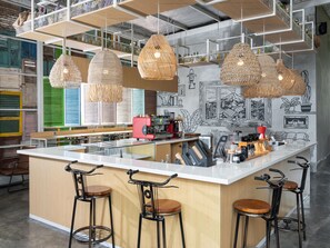 Un espace bar moderne doté d'un îlot central, de tabourets de bar, de suspensions en osier et d'un mur orné d'illustrations en noir et blanc.