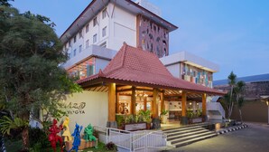 Un hotel de estilo arquitectónico tradicional, con una entrada destacada que presenta un tejado de baldosas y un jardín ajardinado con estatuas.