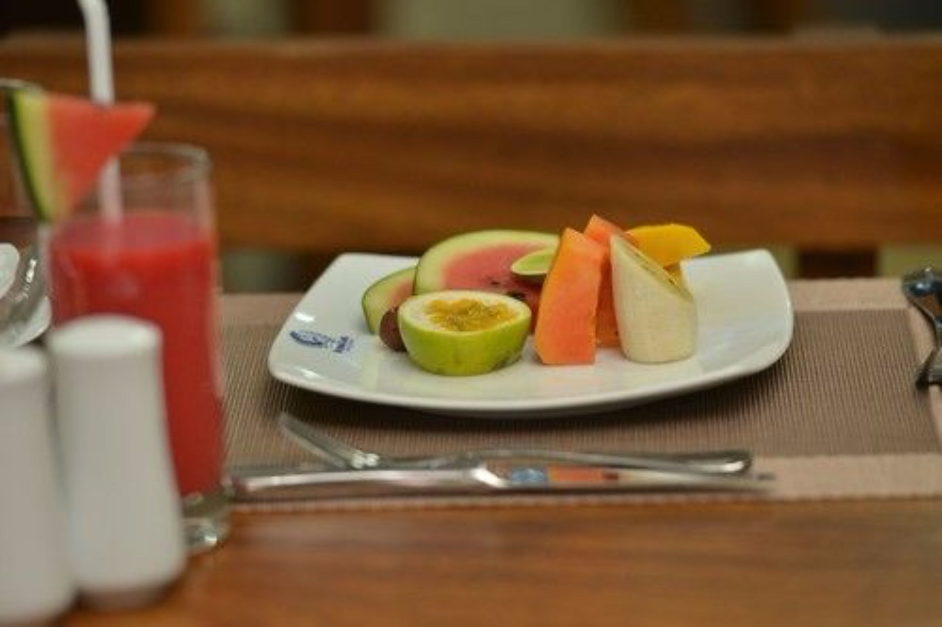Une assiette de fruits coupés et un verre d’une boisson rouge sur une table.
