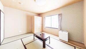 A room with tatami flooring, a low wooden table, a wardrobe, a window with curtains, and a white radiator. - Best Hotel (Tokyo)