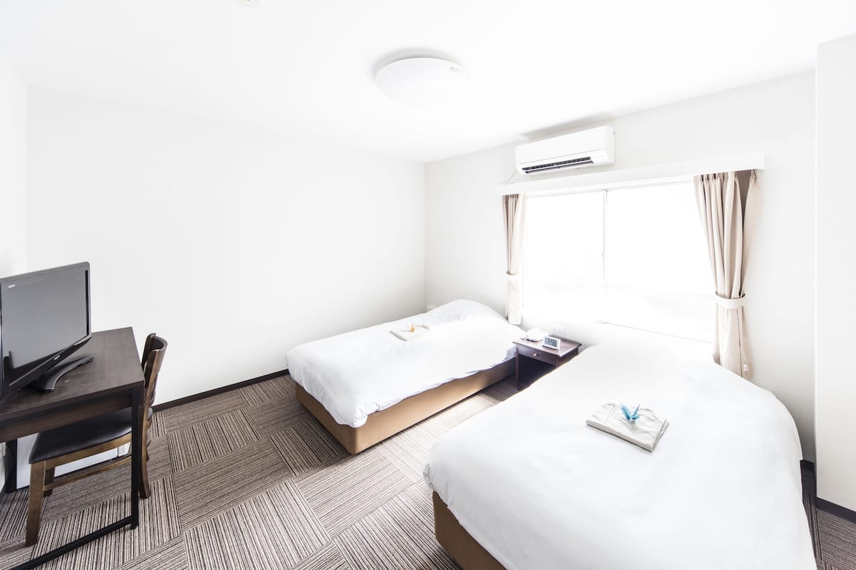 Une chambre d’hôtel avec un lit simple, un bureau avec un ordinateur et une fenêtre avec des rideaux.