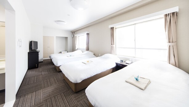 A hotel room with three beds, a flat-screen TV, a desk, and large windows with curtains. - Best Hotel (Tokyo)
