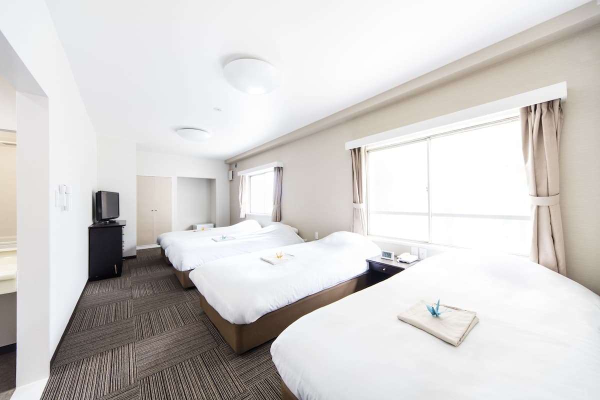 Une chambre d’hôtel avec trois lits, un téléviseur à écran plat, un bureau et de grandes fenêtres équipées de rideaux.