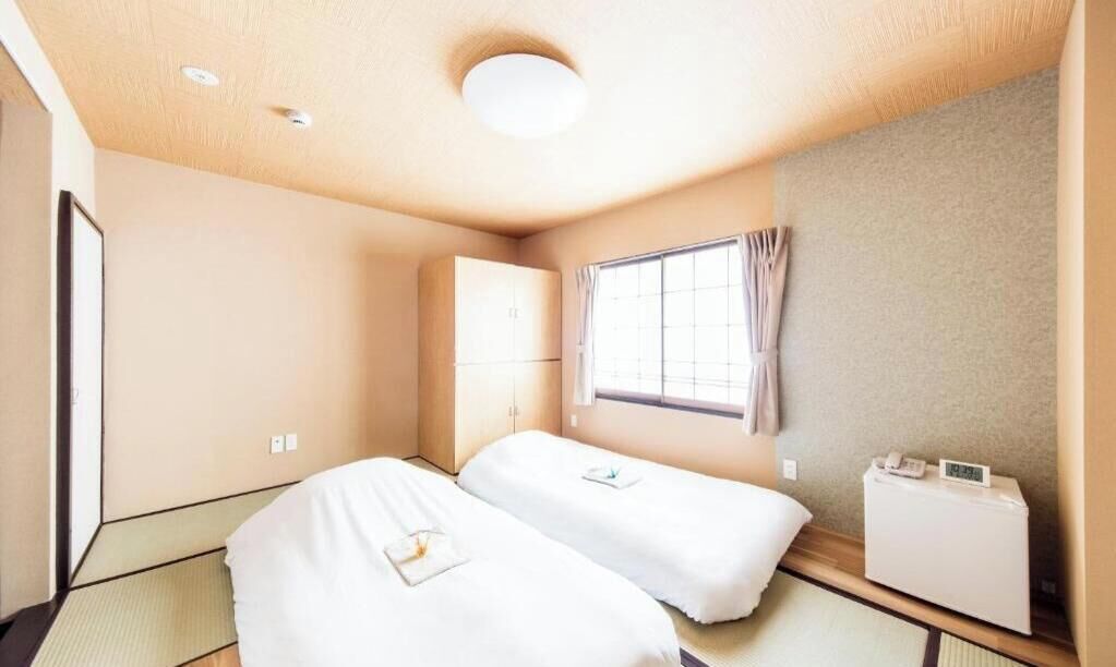 Une chambre d’hôtel avec deux lits, une fenêtre avec des rideaux, une table de chevet avec un téléphone et un radiateur fixé au mur.