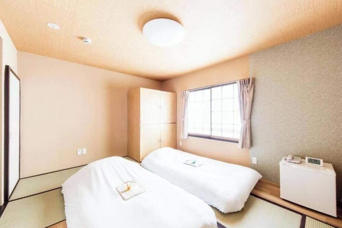 Une chambre d’hôtel avec deux lits, une fenêtre avec des rideaux, une table de chevet avec un téléphone et un radiateur fixé au mur.