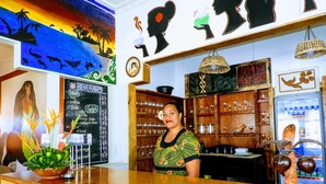 Un área de bar con mostrador de madera, un menú en la pizarra que enumera bebidas y estantes con vasos y botellas.