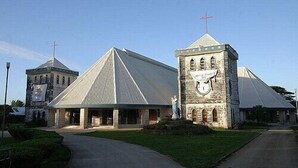 Una iglesia con un techo triangular destacado y una torre de piedra con cruz.