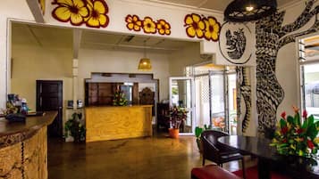 A spacious lobby with a wooden reception desk, a seating area with a red bench, and a large wall mural with floral and tree designs.