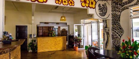 A spacious lobby with a wooden reception desk, a seating area with a red bench, and a large wall mural with floral and tree designs.