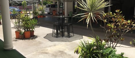 An outdoor patio area with a table and chairs, surrounded by potted plants and umbrellas.
