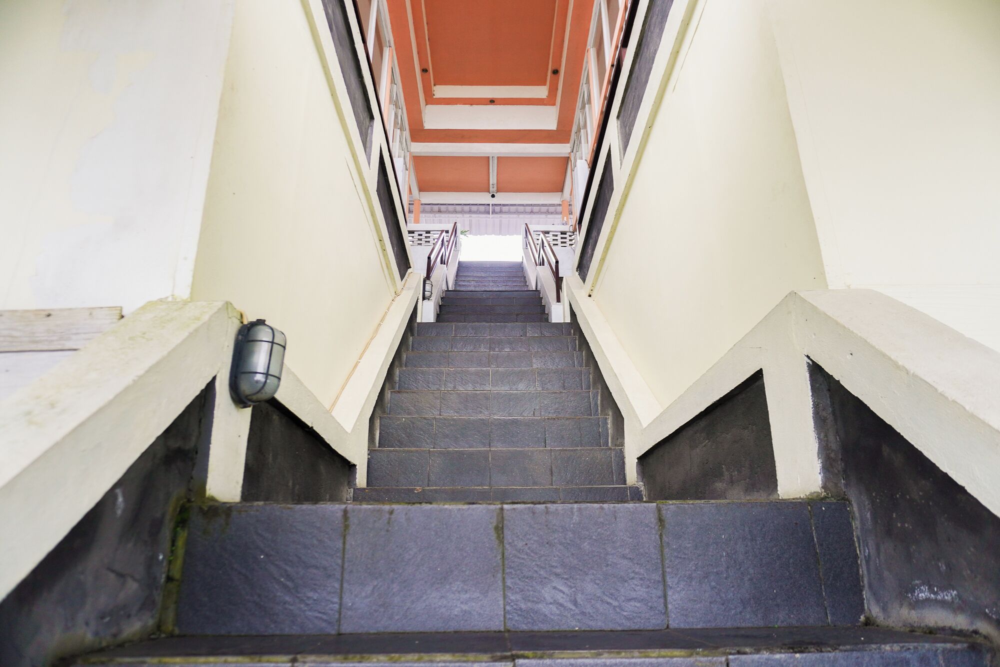 A staircase with a handrail on both sides, leading to a landing with a light-colored wall and a dark-colored ceiling.