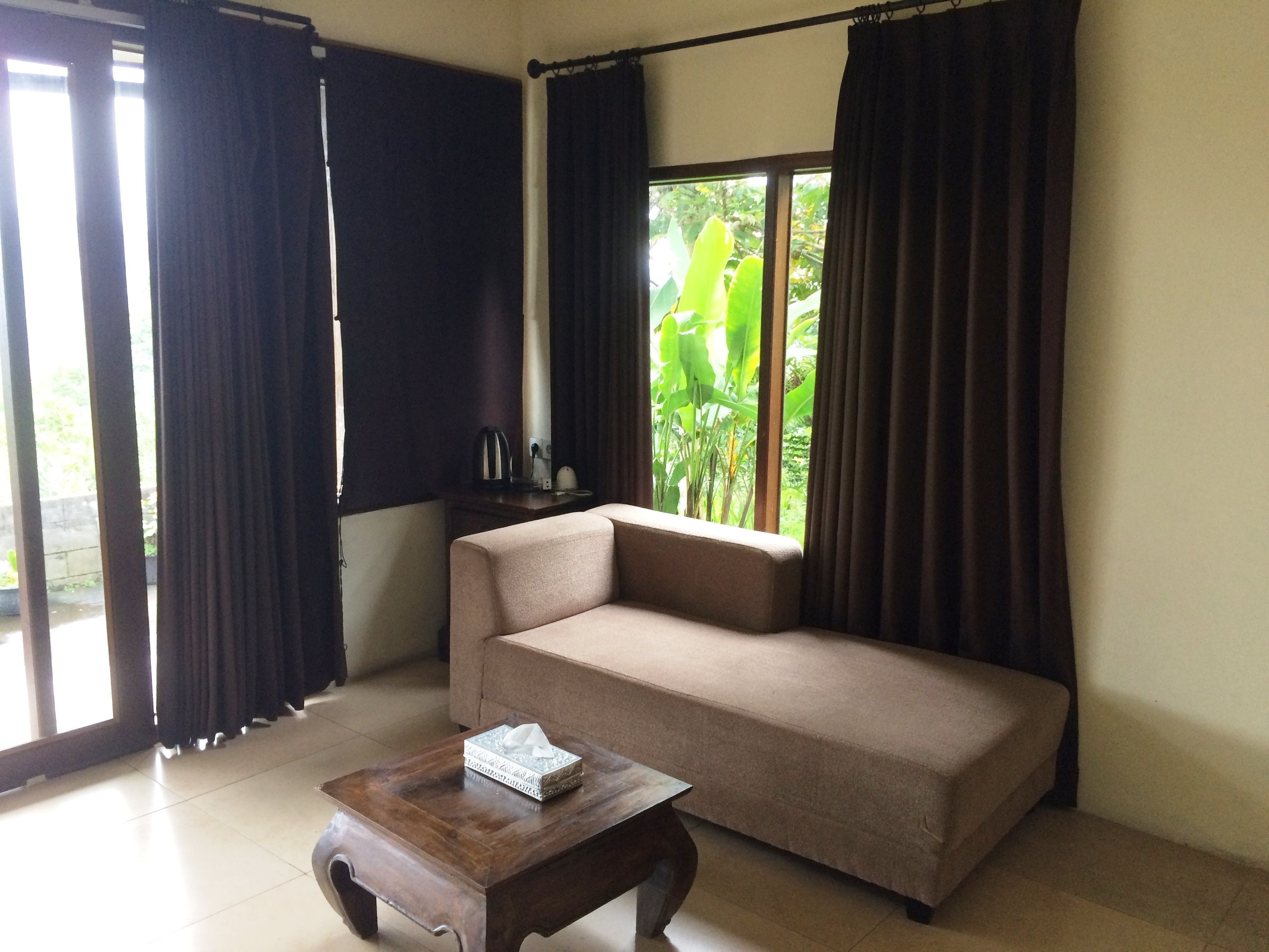 A living room with a beige sofa, a wooden coffee table, and a window with curtains.