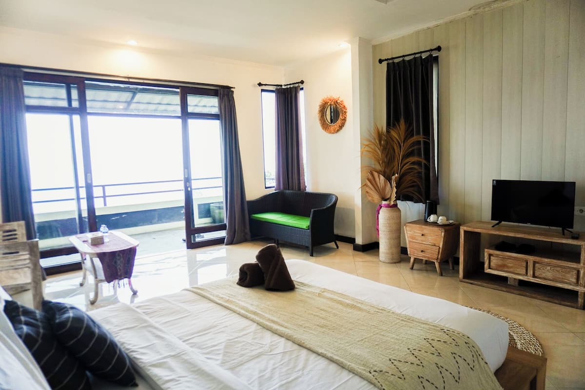 Quarto de hotel com cama, televisão, sofá, mesa pequena e varanda com vista.
