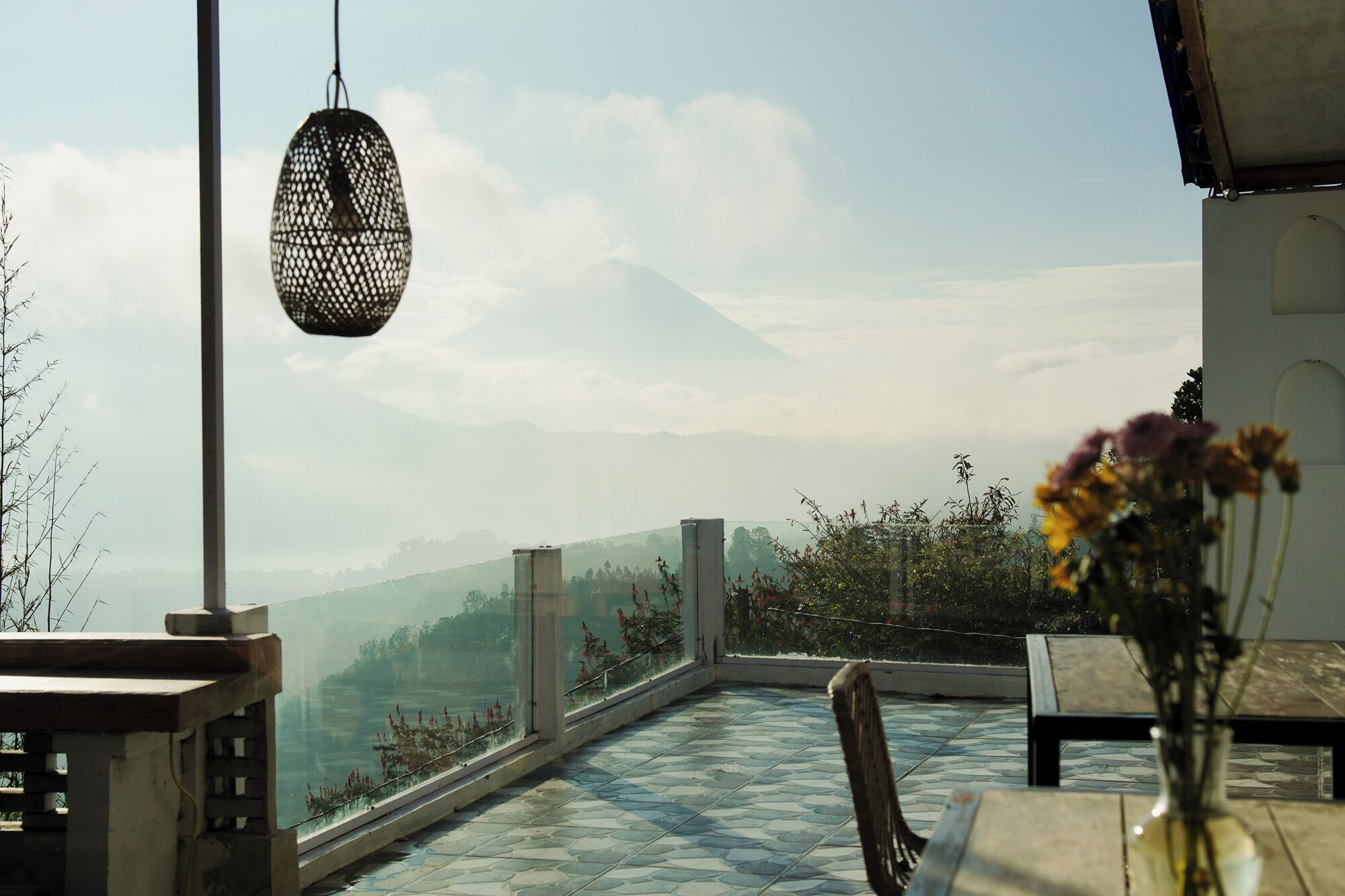 A terrace with a view of a mountain, a hanging light fixture, and a table with a vase of flowers.