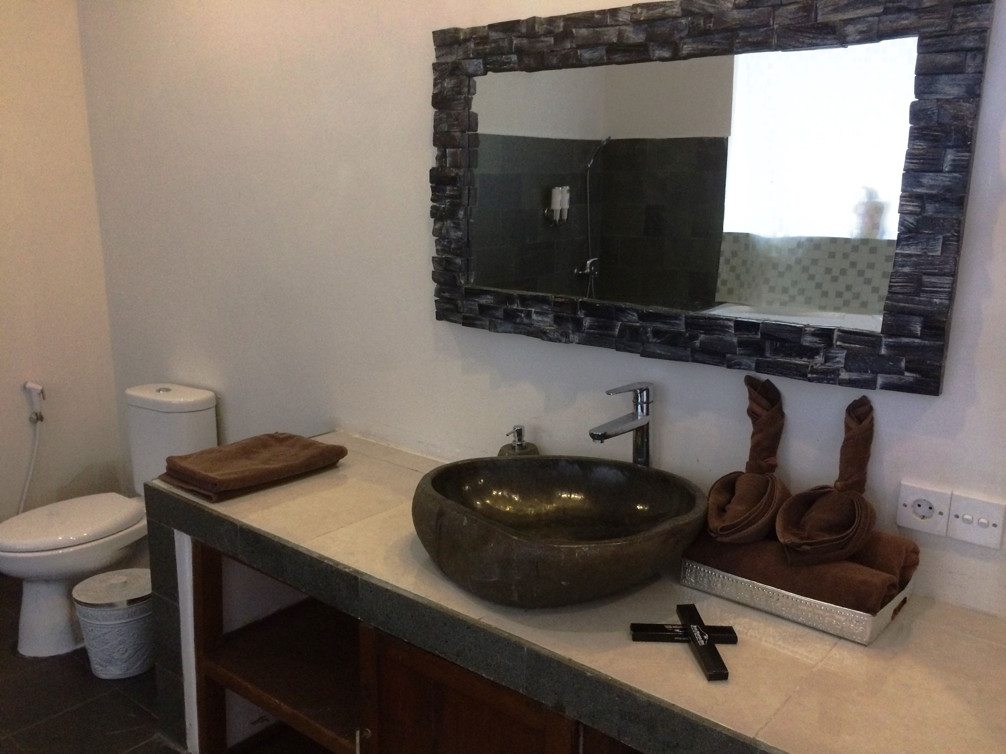 Ein Badezimmer mit einem Steinklopfbac, einem Spiegel mit Steingestell, einer Toilette und einem Handtuchhalter mit Handtüchern.