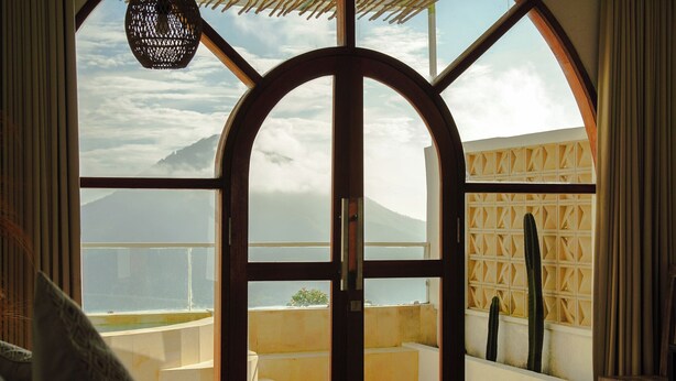 A room with a large arched window overlooking a mountainous landscape.