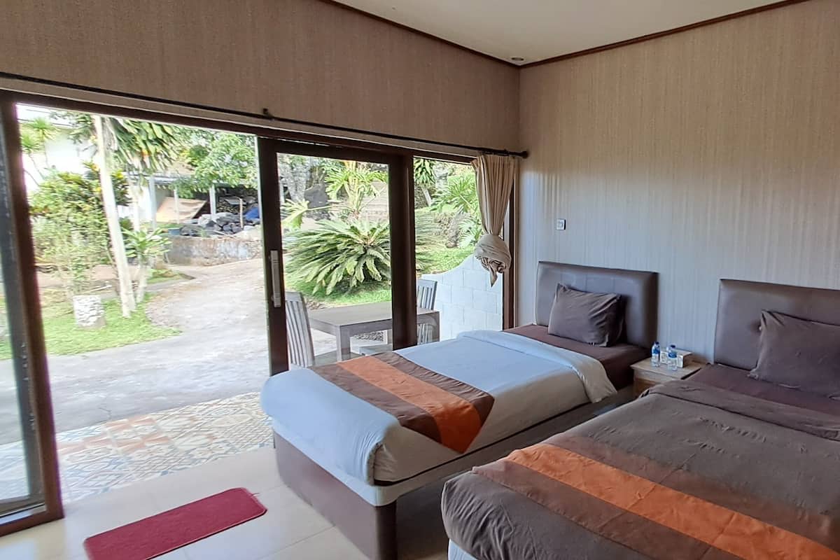 Quarto com duas camas, porta de vidro deslizante para o exterior e uma mesinha com uma garrafa de água.