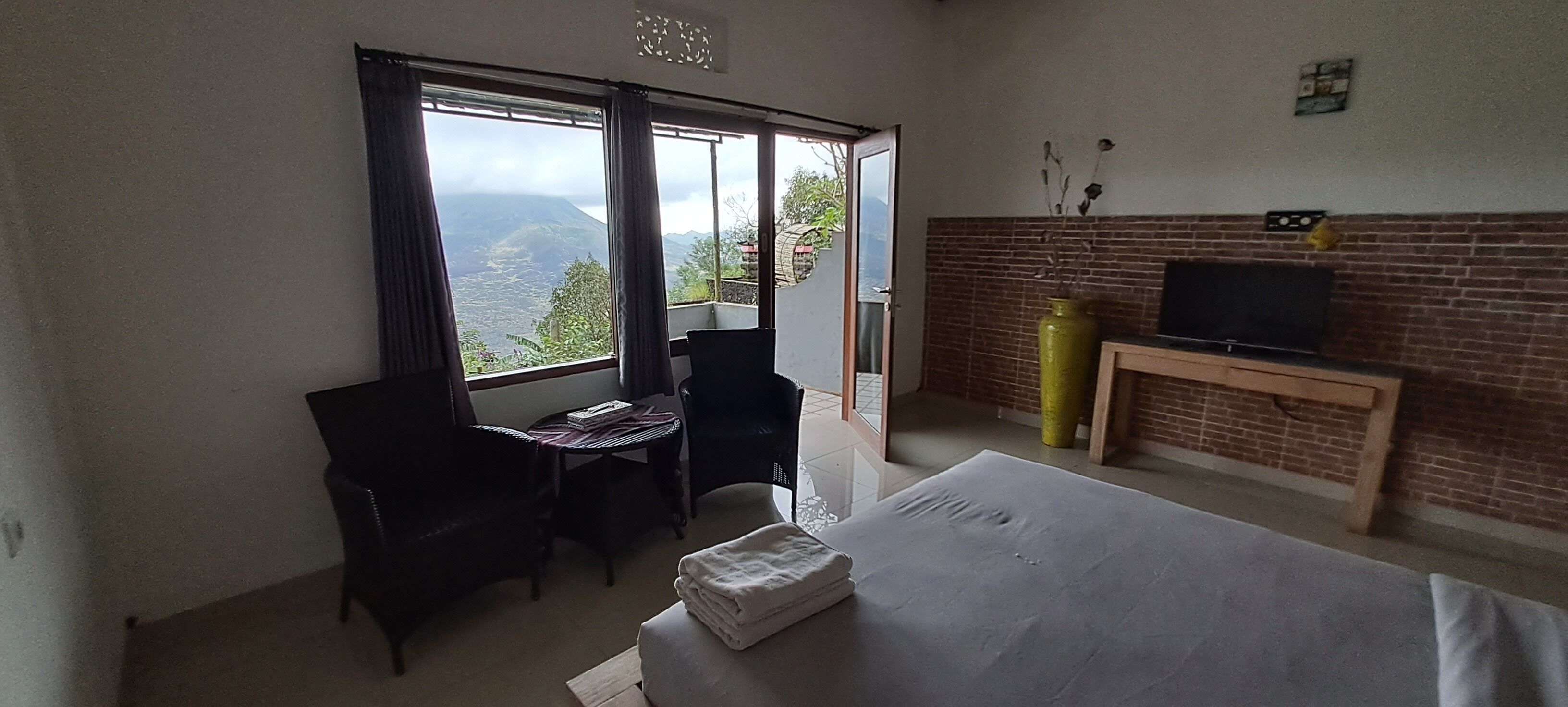 Camera d'albergo con un letto, una TV, un camino in mattoni, una finestra con tende e vista sulle montagne.