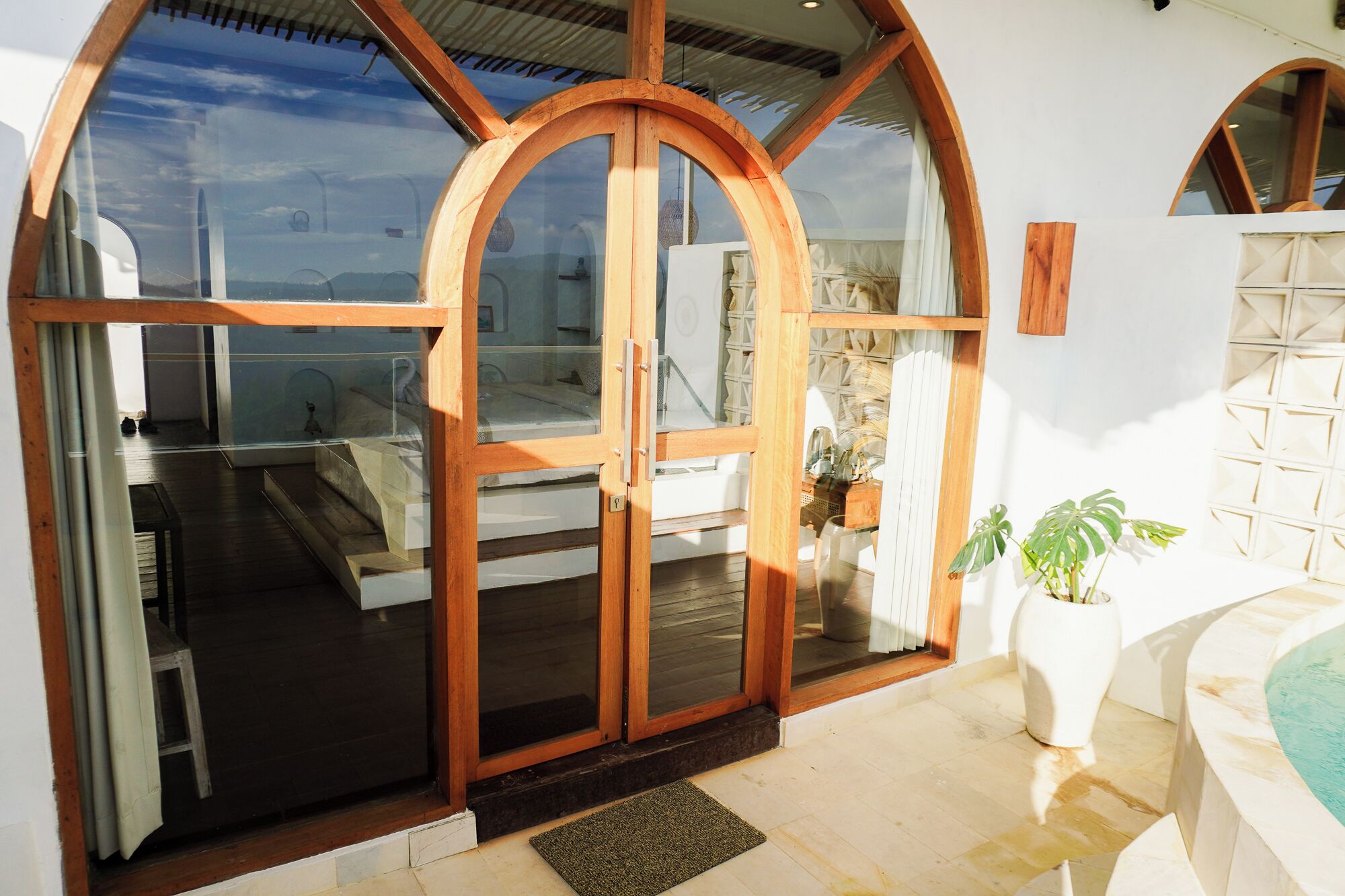 A modern room with a glass door entrance, a bed, a small table, and a potted plant.
