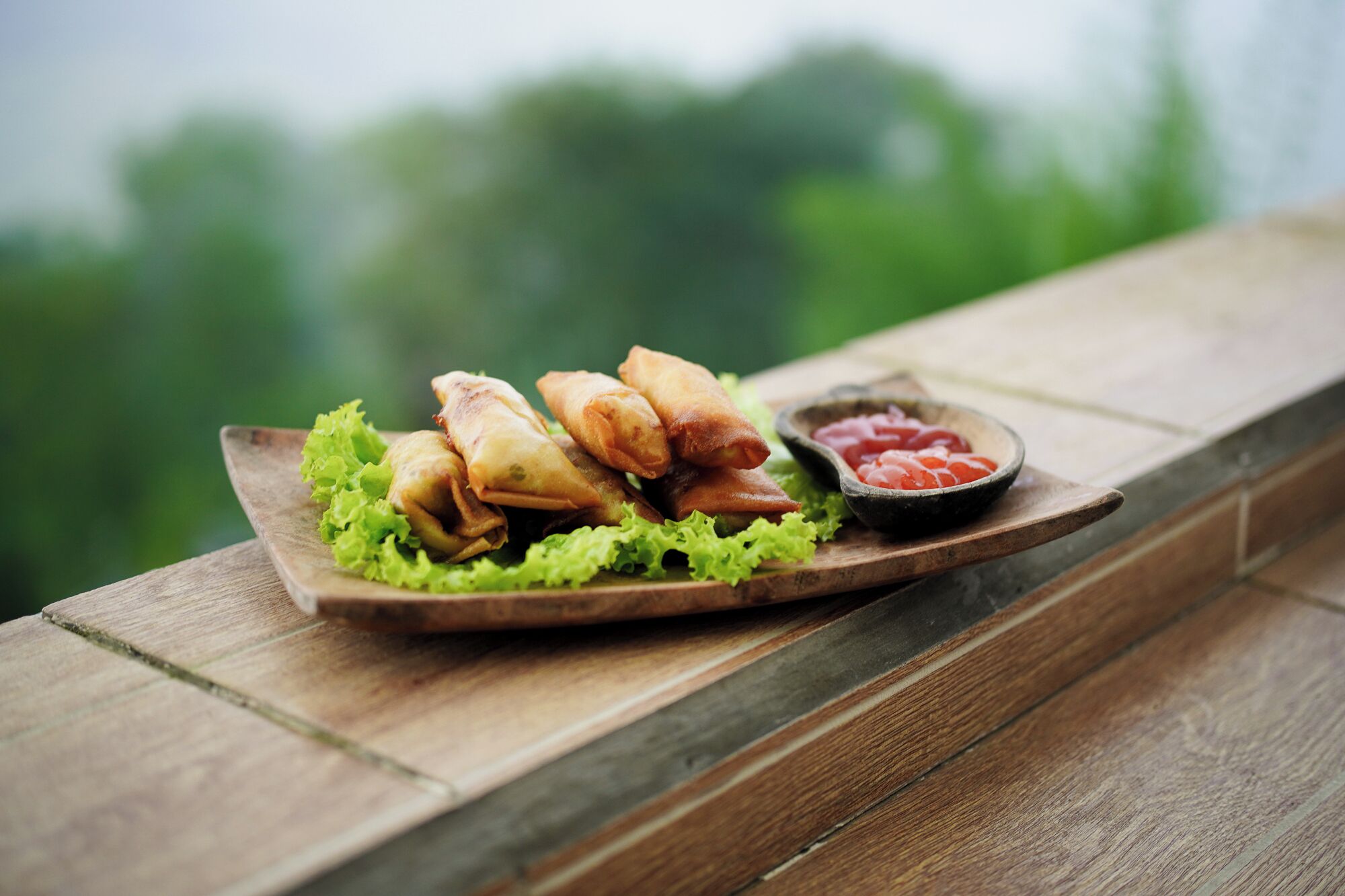 A wooden table with a plate of spring rolls and a small bowl of ketchup.