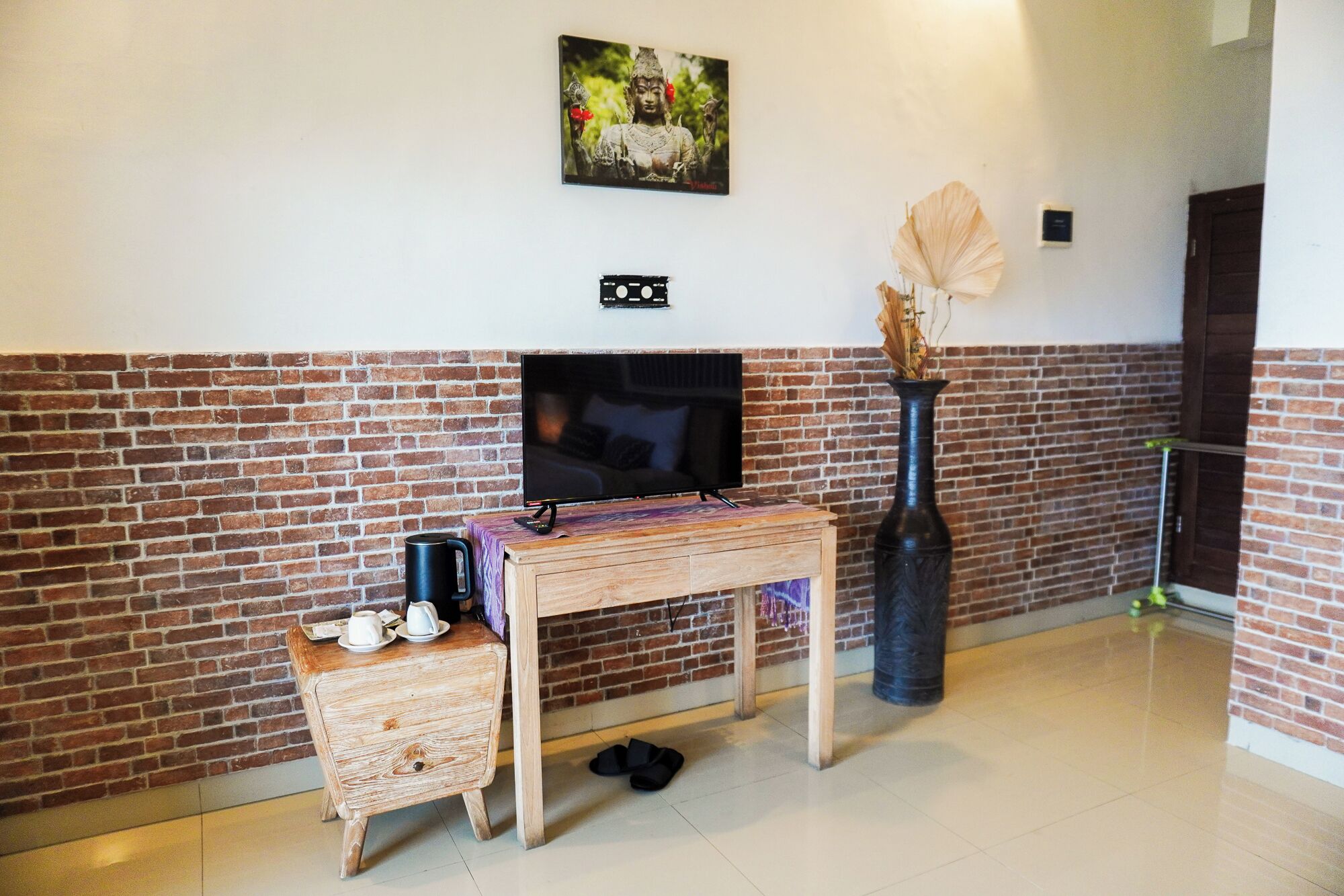 A living room with a TV, a coffee table, a decorative vase, and a brick wall.