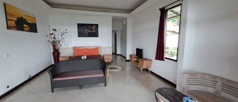 Un espacio habitable amplio con un sofá, un banco de madera, un mueble para televisión y obras de arte en las paredes.