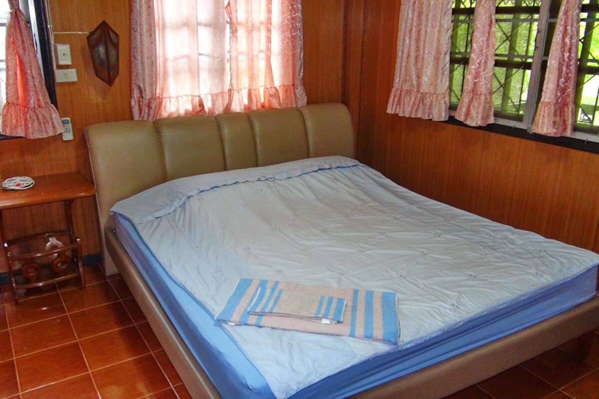 A room with a bed, a wooden bench, a small table, and a window with curtains.