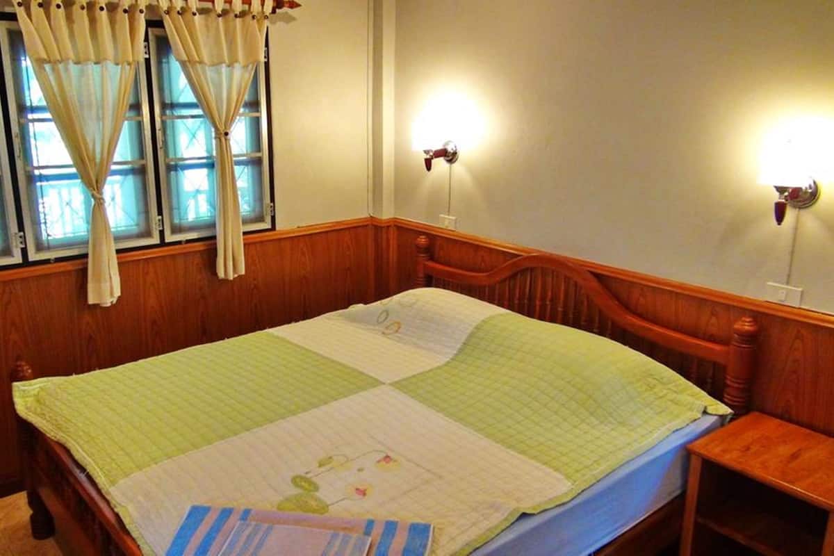 A bedroom with a wooden bed, a nightstand, and a window with curtains.
