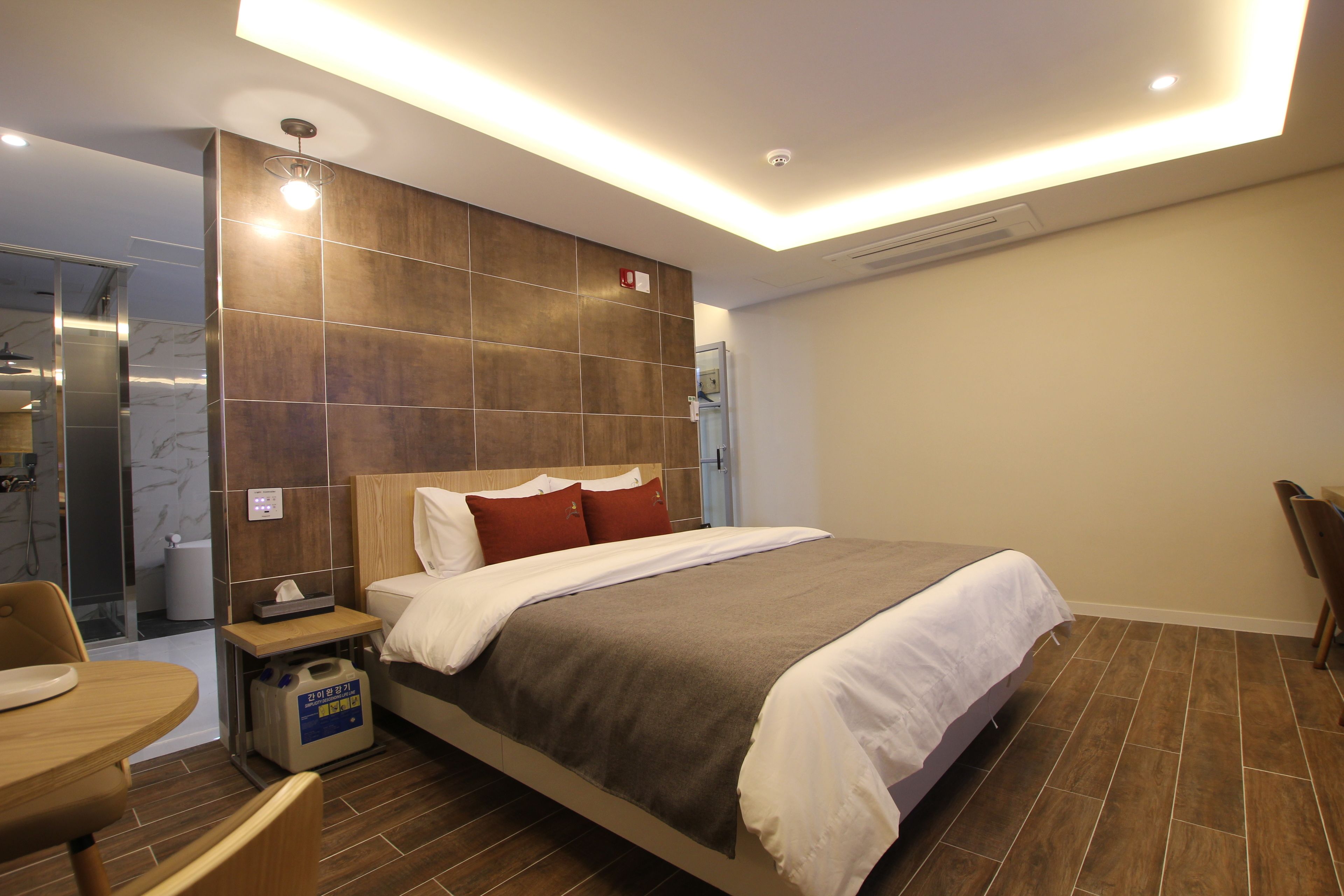 A modern hotel room with a large bed, a bedside table, a chair, and a small table.