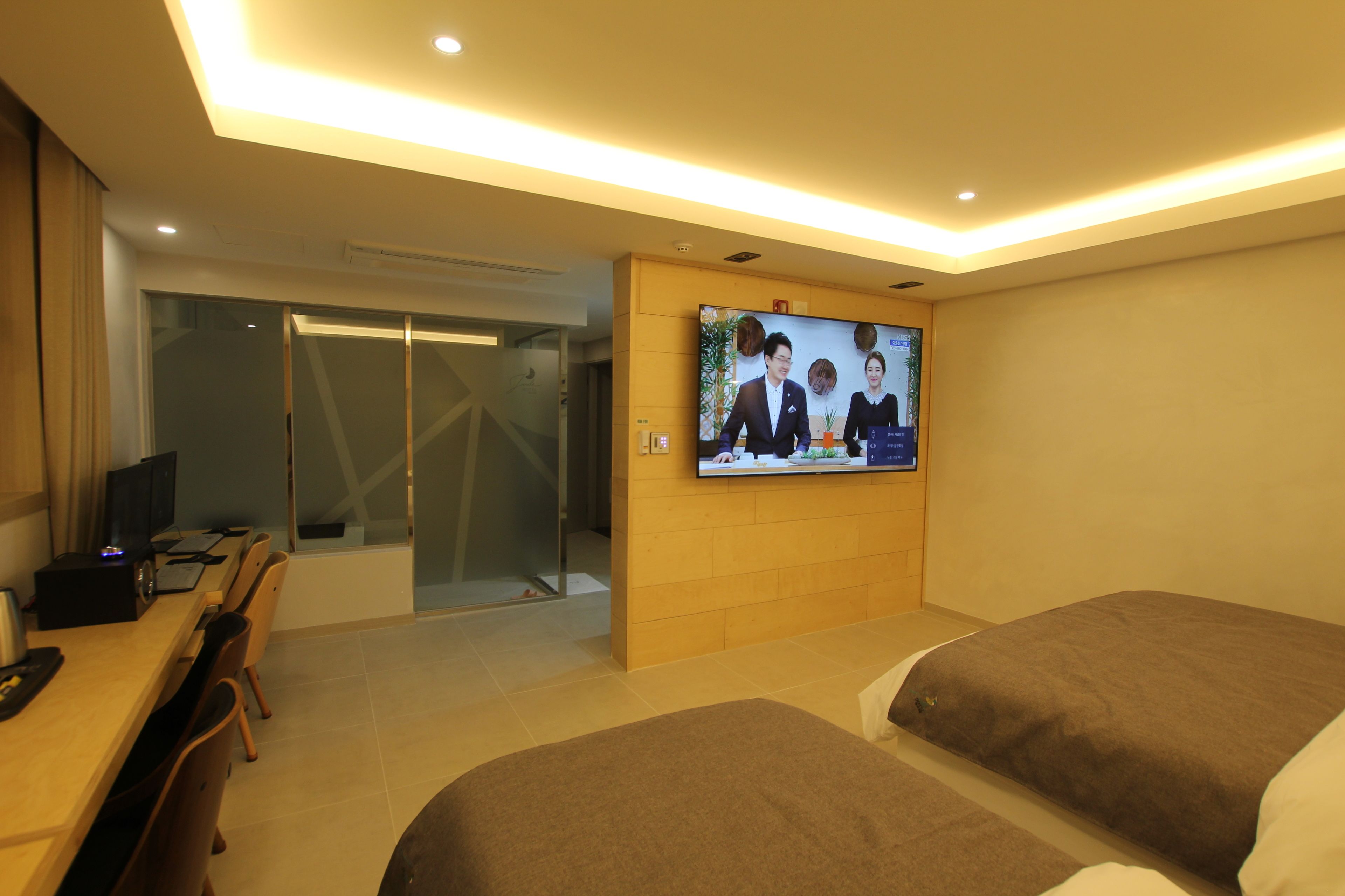 A hotel room with a TV on the wall, a desk with a computer, and two beds.