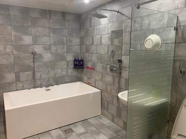 A modern bathroom with a large bathtub, a glass-enclosed shower, and grey tiled walls. - Jade Hotel Ulsan (Ulsan)