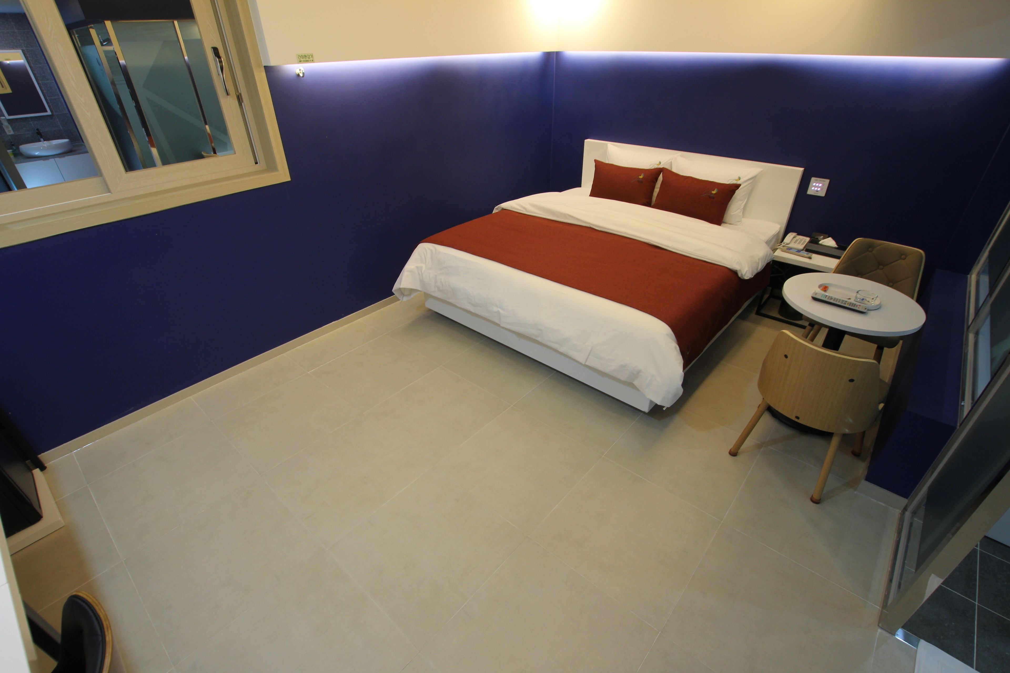 A hotel room with a bed, a small table with a chair, and a window.