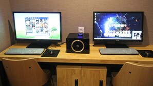 Two monitors on a wooden desk with a keyboard and mouse, and a speaker in the center. - Jade Hotel Ulsan (Ulsan)