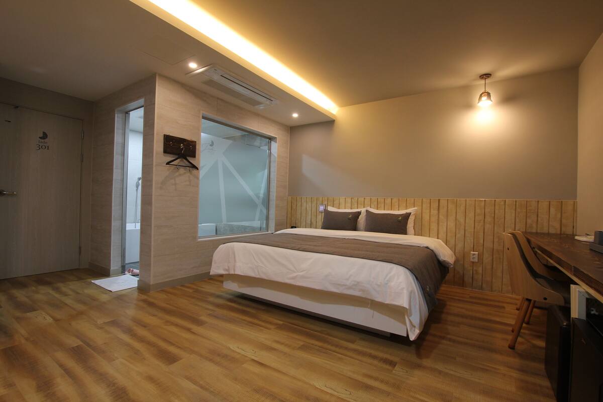 Un dormitorio moderno con suelo de madera, una cama con ropa de cama blanca y marrón, un escritorio y una lámpara colgante.
